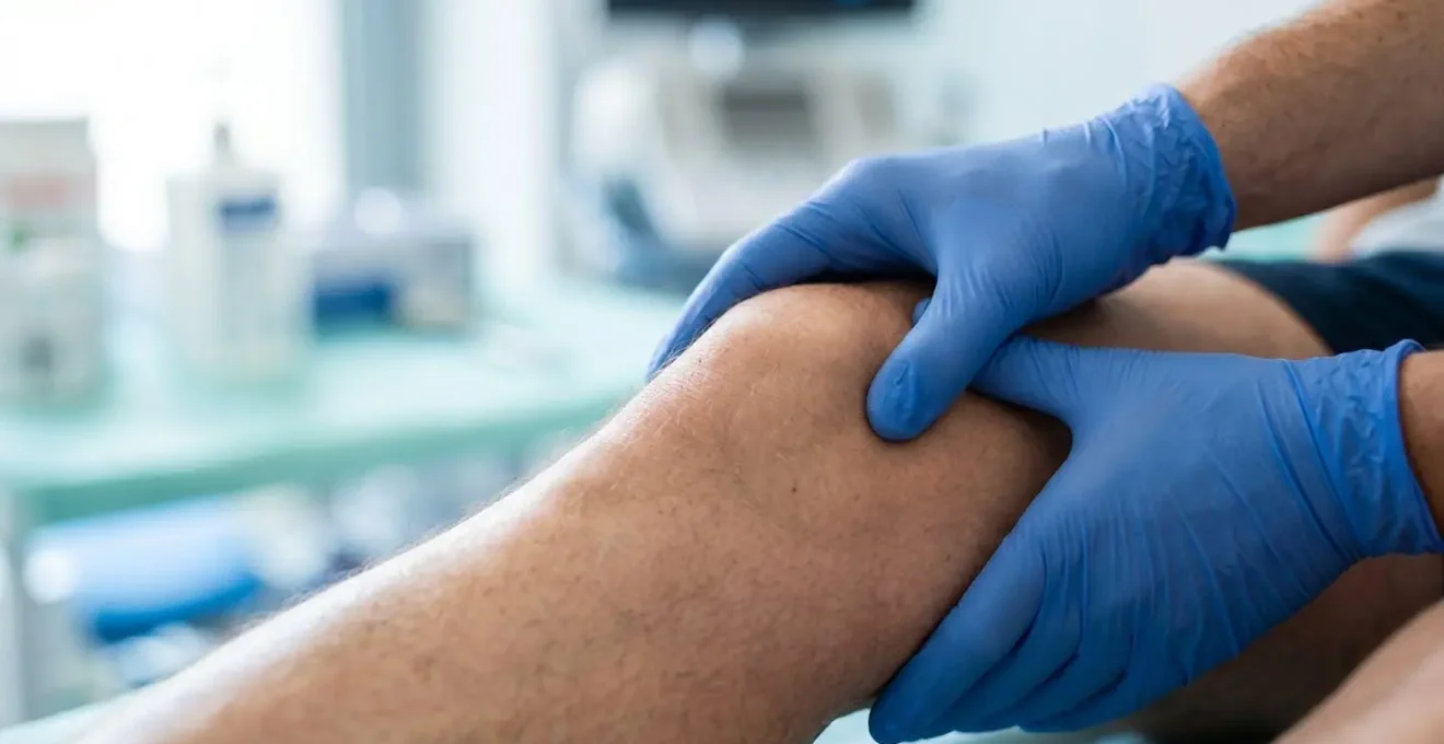 Gros plan sur les mains d'un professionnel de santé palpant le genou d'un patient lors d'un examen clinique